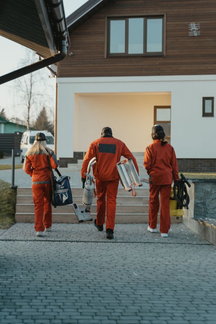Une équipe de nettoyage en uniforme rouge, munie de son matériel, s’approche de l’extérieur d’une maison moderne.
